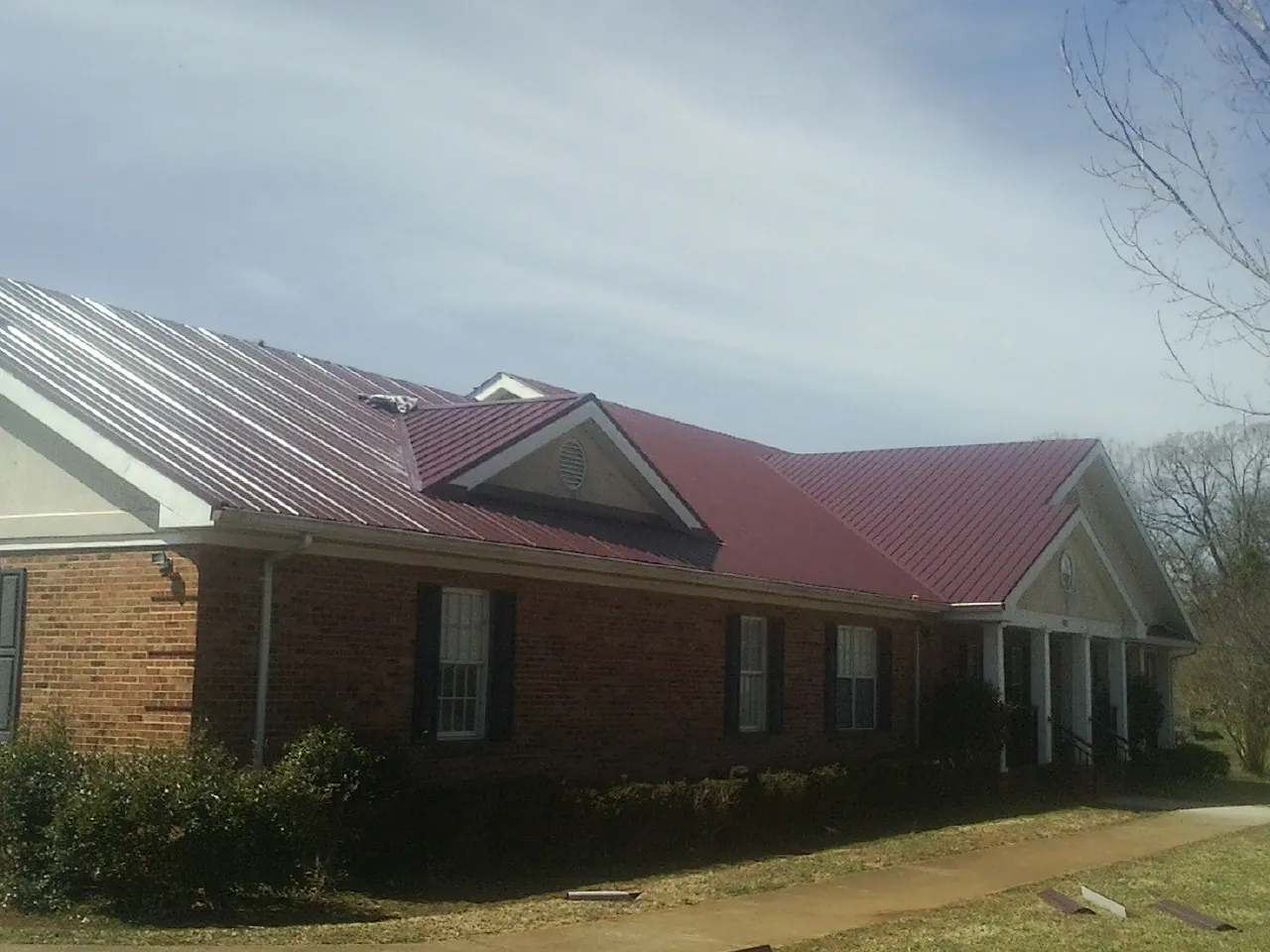Red metal roof with gabled entries on a long brick building, from a Hail Damage Roof Repair job in Granby