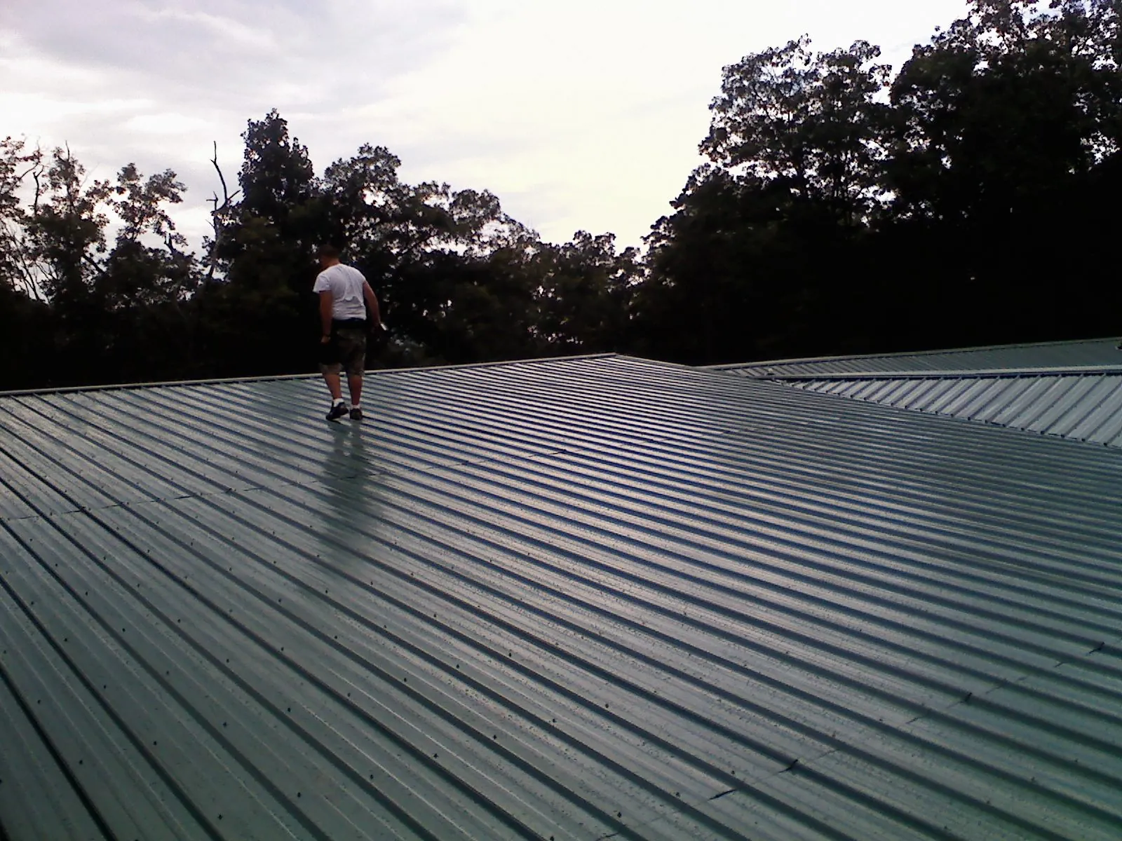 Roofer walking a wide expanse of new green metal roofing in Granby