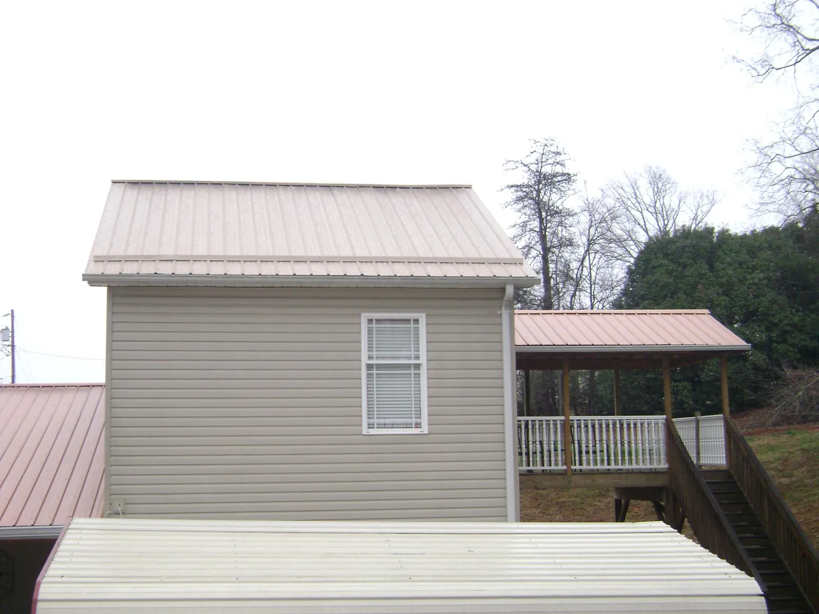 Tan metal roofs on a two story addition and attached porch, from a Roof Replacement job in Granby
